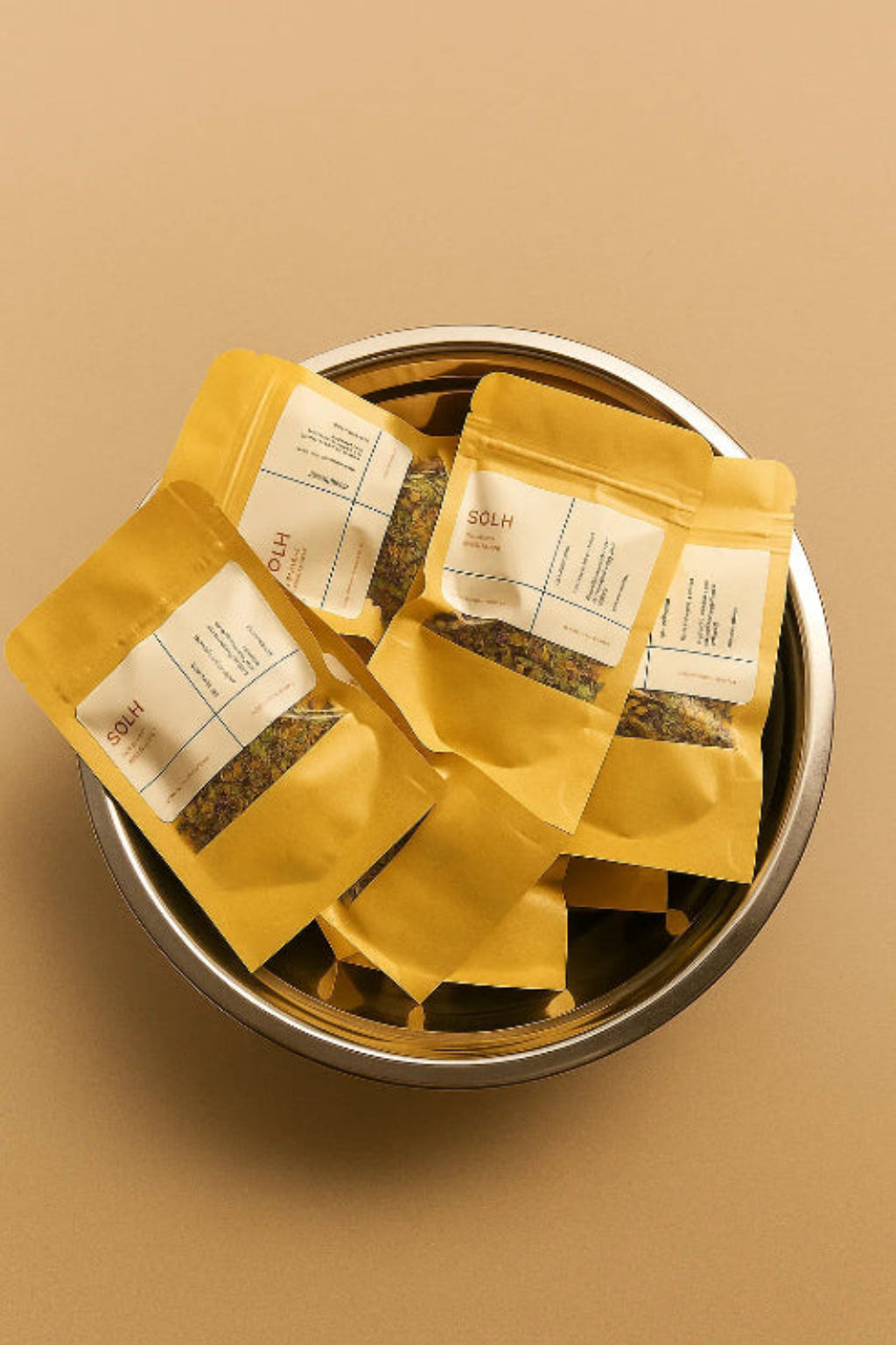 Three yellow packages of tea in a metal bowl on a beige background